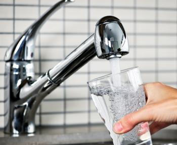 person filling a glass up with water from a tap